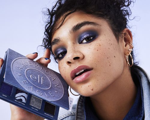 A model wearing blue eyeshadow and holding the AE x e.l.f Eyeshadow Palette