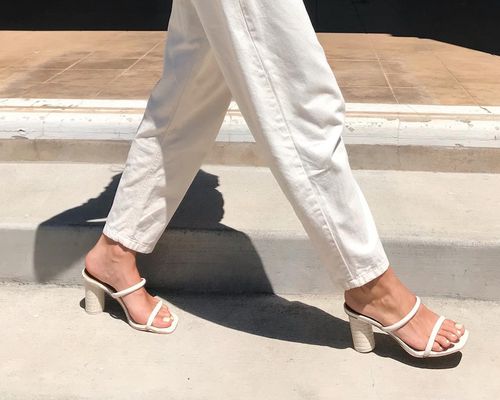 Close-up of woman walking wearing white denim pants and open-toe heels