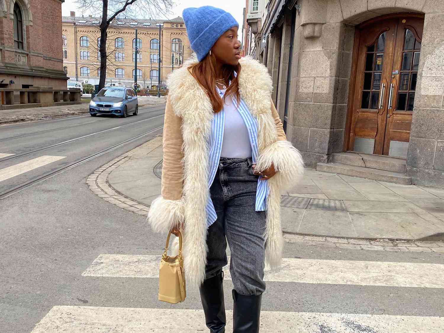 Norwegian fashion influencer Nnenna Echem wears a shearling coat, striped button-down, beanie, and jeans