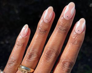 Manicure with translucent neutral base, white art deco design, and small rhinestone accents