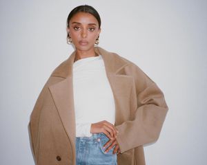 Woman wearing white shirt, jeans, camel coat, and gold hoop earrings