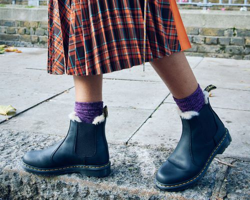 Doc Martens shearling-lined chelsea boots with purple knit socks and an orange plaid skirt