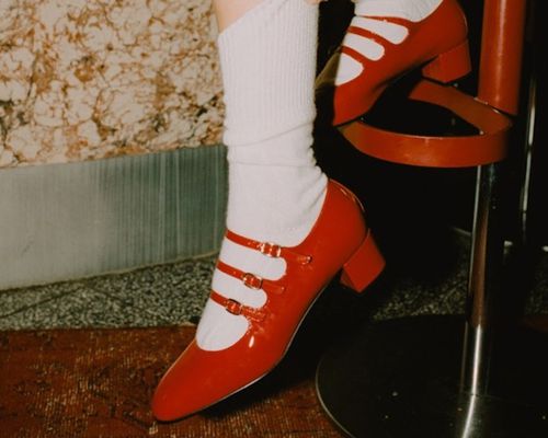 Close-up of woman pulling up crew socks paired with red Carel heeled Mary Jane shoes