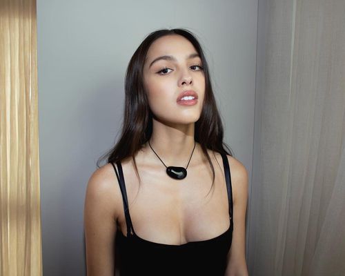 Olivia Rodrigo wears a black tank top and string necklace with large pendant