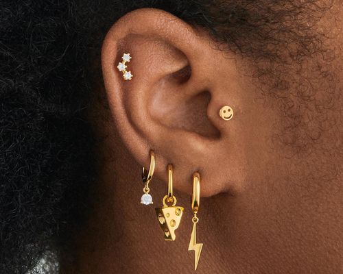 close up of woman's ear featuring many different gold piercings