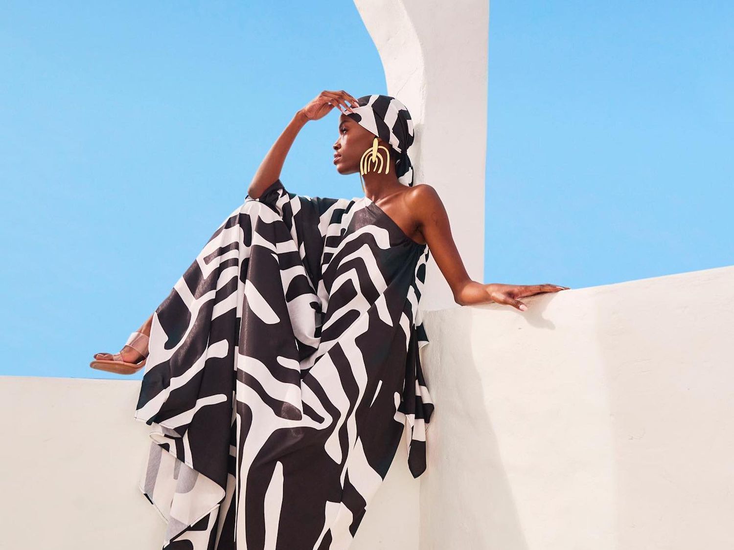 Woman sitting on balcony in sunshine wearing black and white dress and headscarf