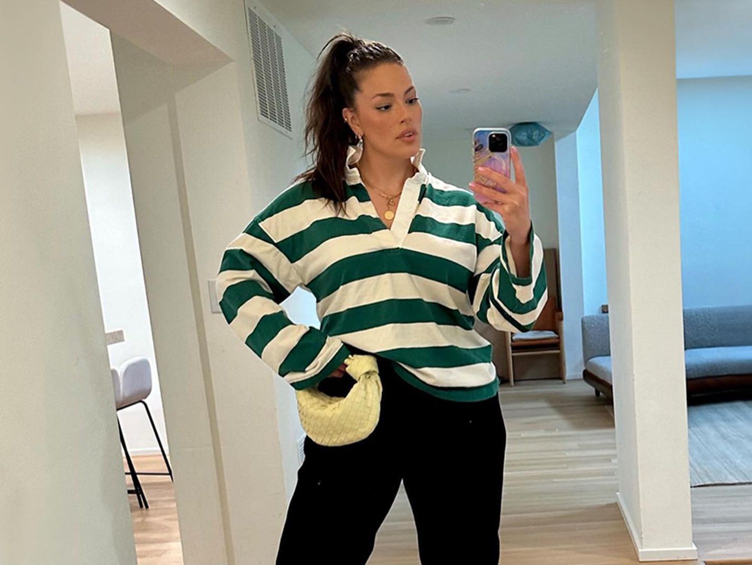 Ashley Graham wears a green and white striped rugby shirt, yellow knotted Bottega Veneta bag, and black wide leg pants