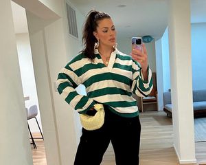 Ashley Graham wears a green and white striped rugby shirt, yellow knotted Bottega Veneta bag, and black wide leg pants