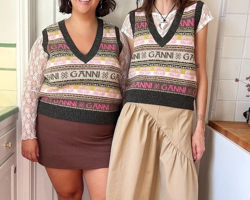 Two women wearing Ganni striped logo sweater vests, white lacy tops, and neutral skirts