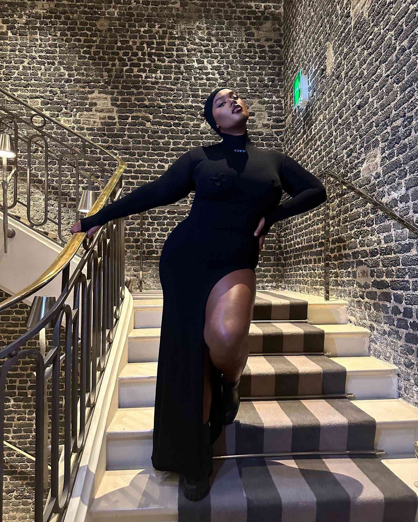 Precious Lee wears a black turtleneck dress while standing on steps