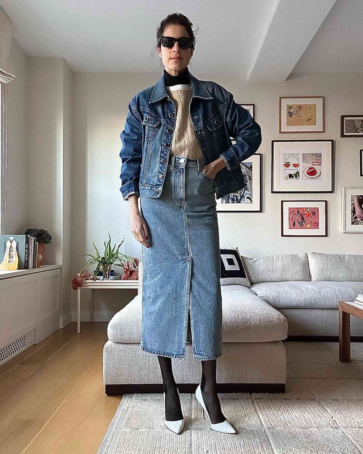 Leandra Medine Cohen wears a neutral sweater, denim jacket and midi skirt, black tights, white pointed-toe heels, and sunglasses