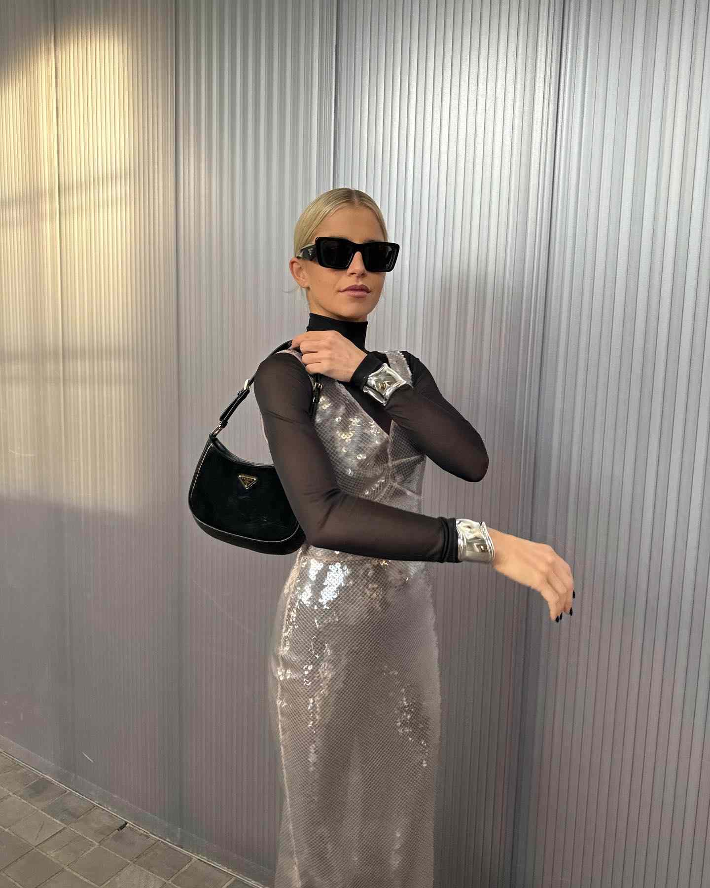 Caroline Daur wears a silver sequined dress, black turtleneck, black Prada bag, and sunglasses