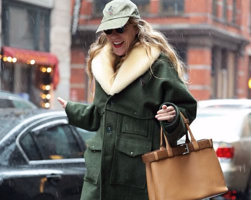 Chloe Sevigny wears a green jacket with shearling trim, tan leather handbag, and Mickey Mouse baseball cap while out in rain