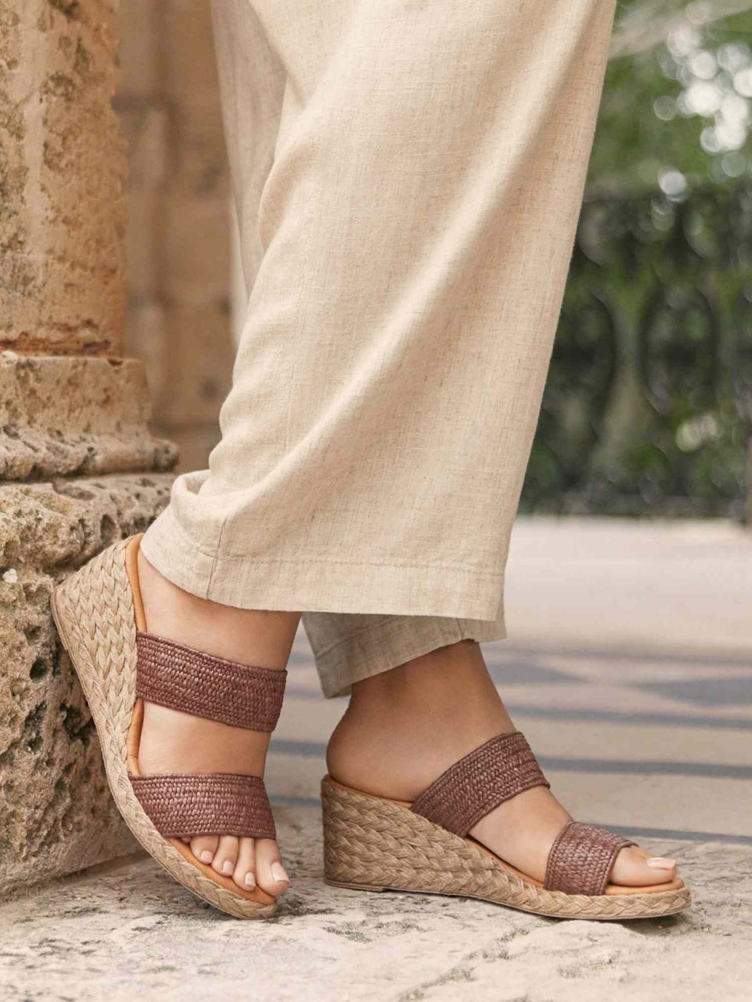 Close-up of person wearing brown wedge sandals with woven platform and beige linen pants