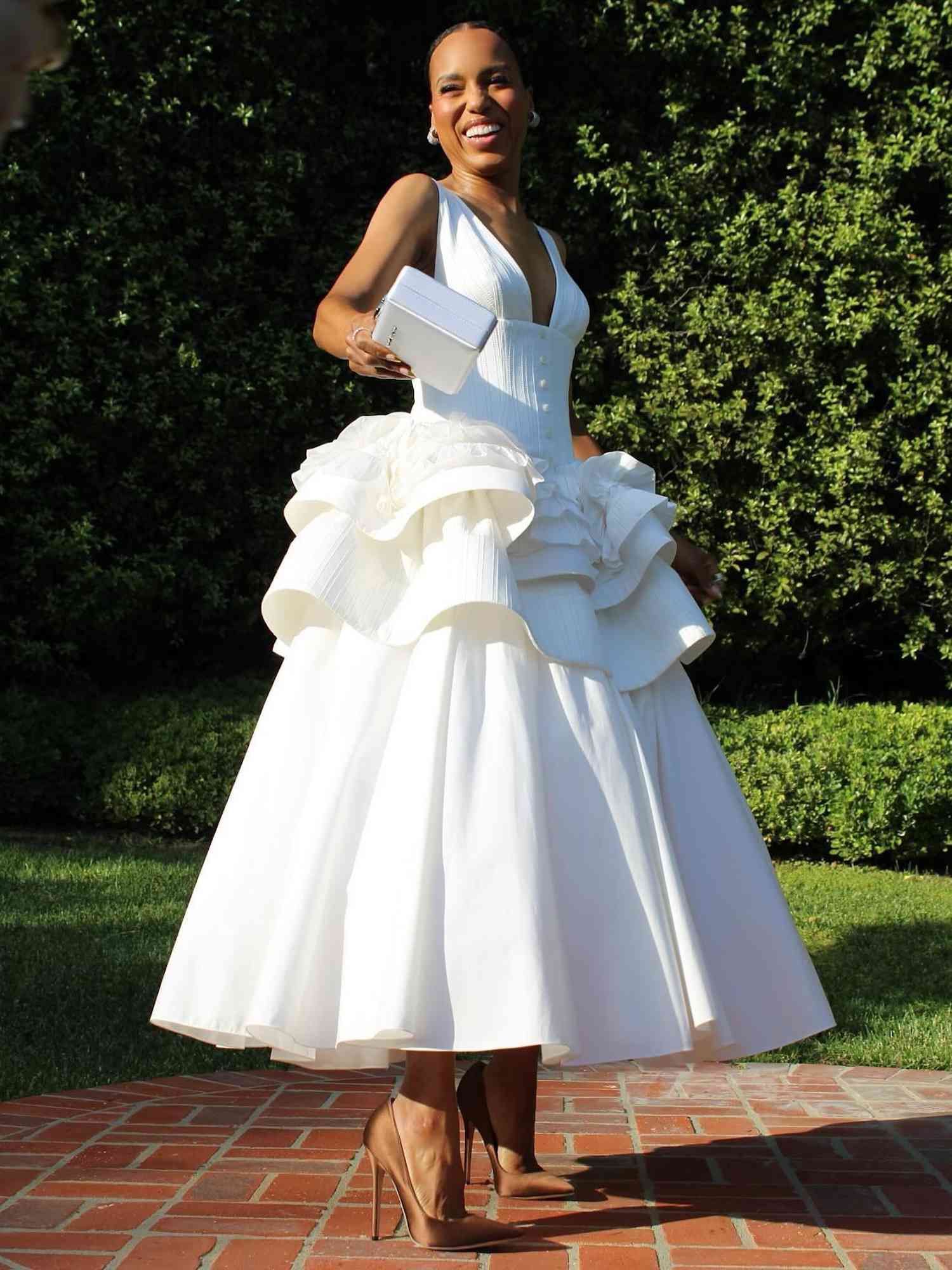 Kerry Washington wears a white Christopher John Rogers dress with ruffled waist, hard-sided handbag, and nude heels