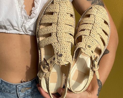 Close-up of woman holding woven fisherman sandals while wearing white crop top and jeans