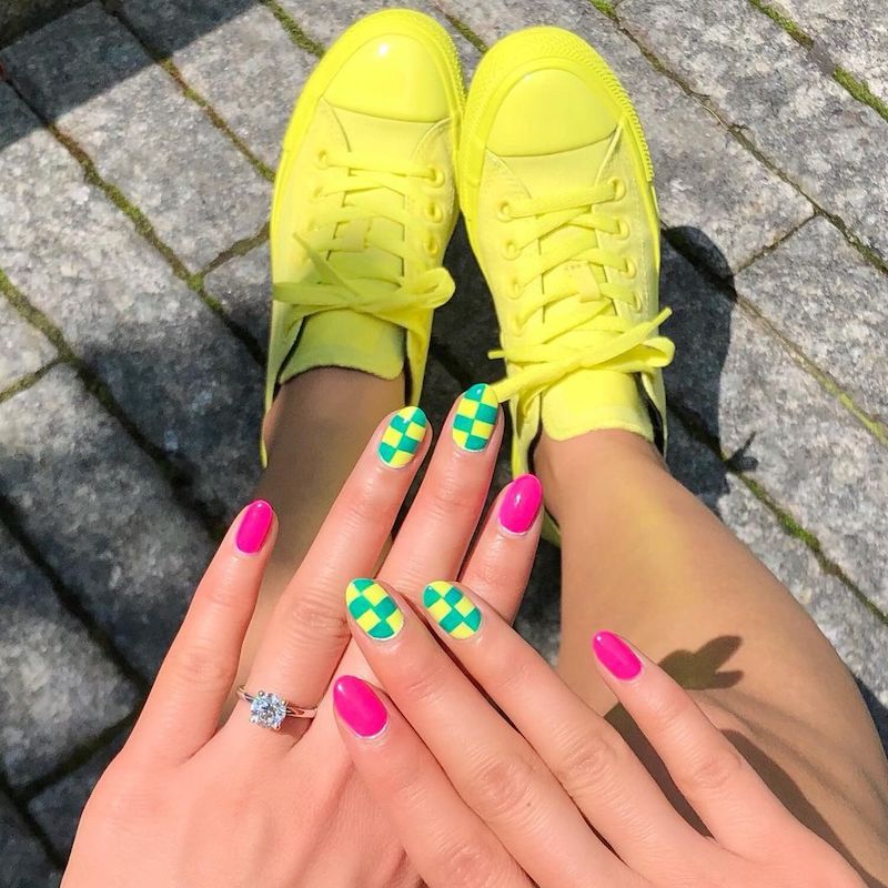 Neon pink and green checkerboard manicure in front of bright yellow hightops