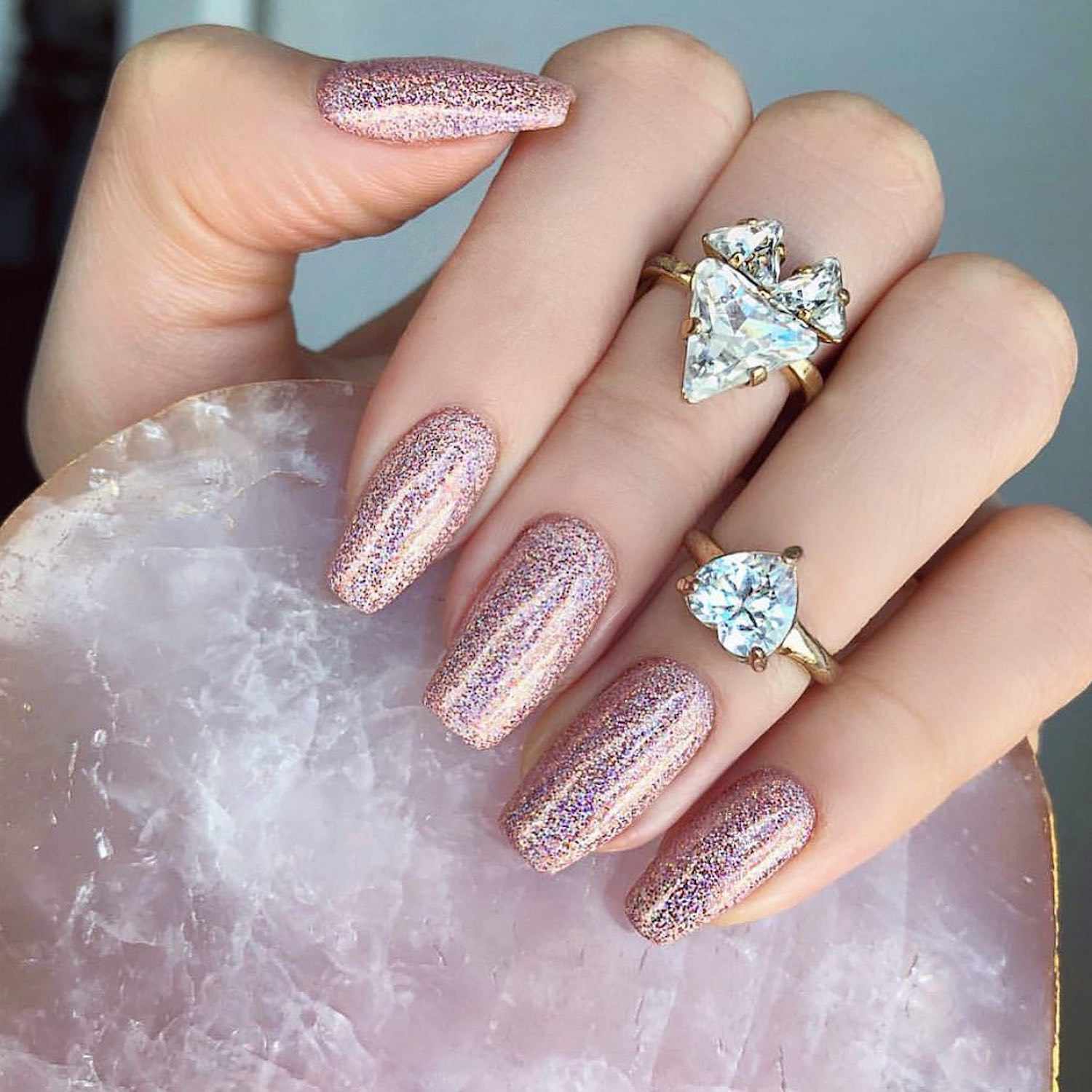 Hand with rose gold glitter manicure holding rose quartz