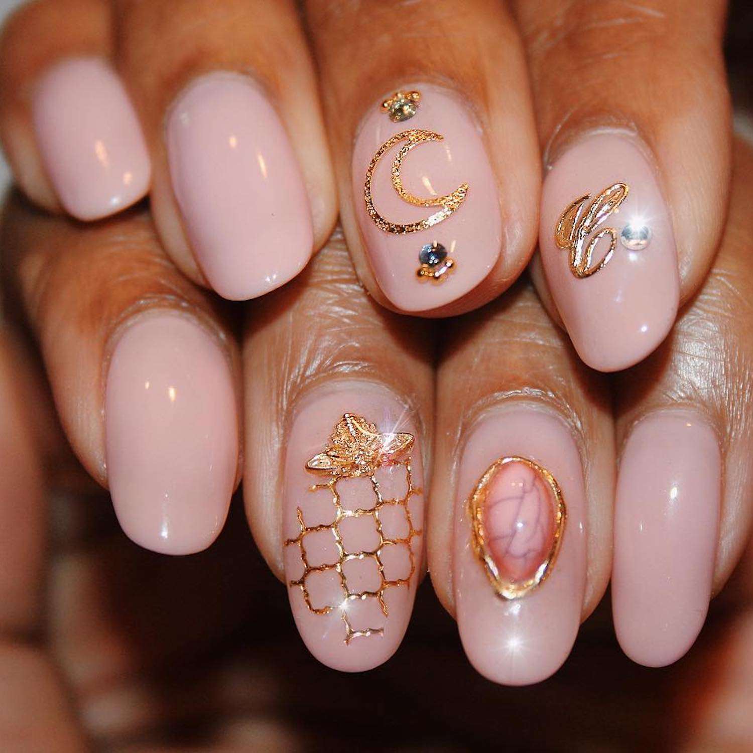 Peachy nude manicure with rose gold moon, initial, ring, and spaceship nail designs