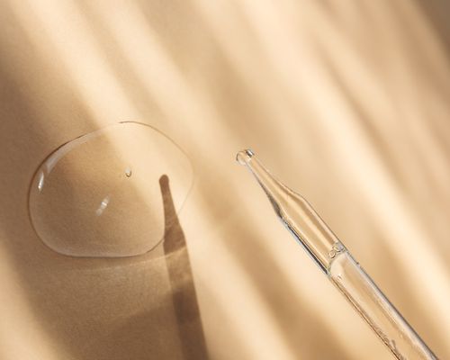 close up of dropper bottle with clear liquid on tan background