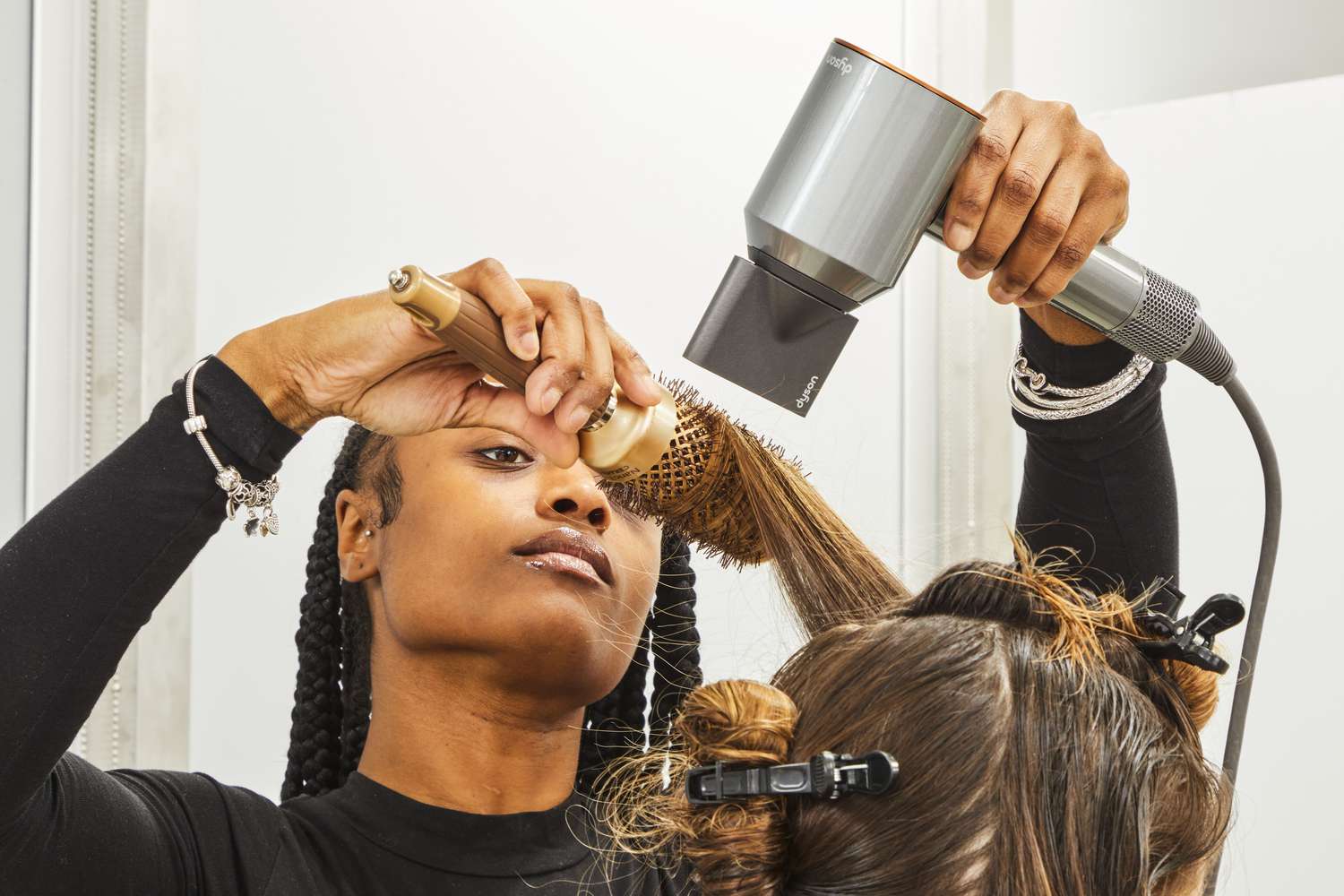 Woman using a Dyson Supersonic Hair Dryer on another persons hair with a brush