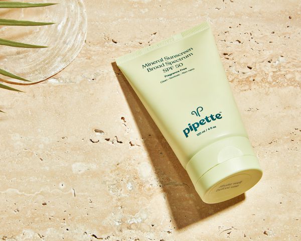 Pipette Mineral Sunscreen displayed on a sandy background next to a leafy plant and seashell