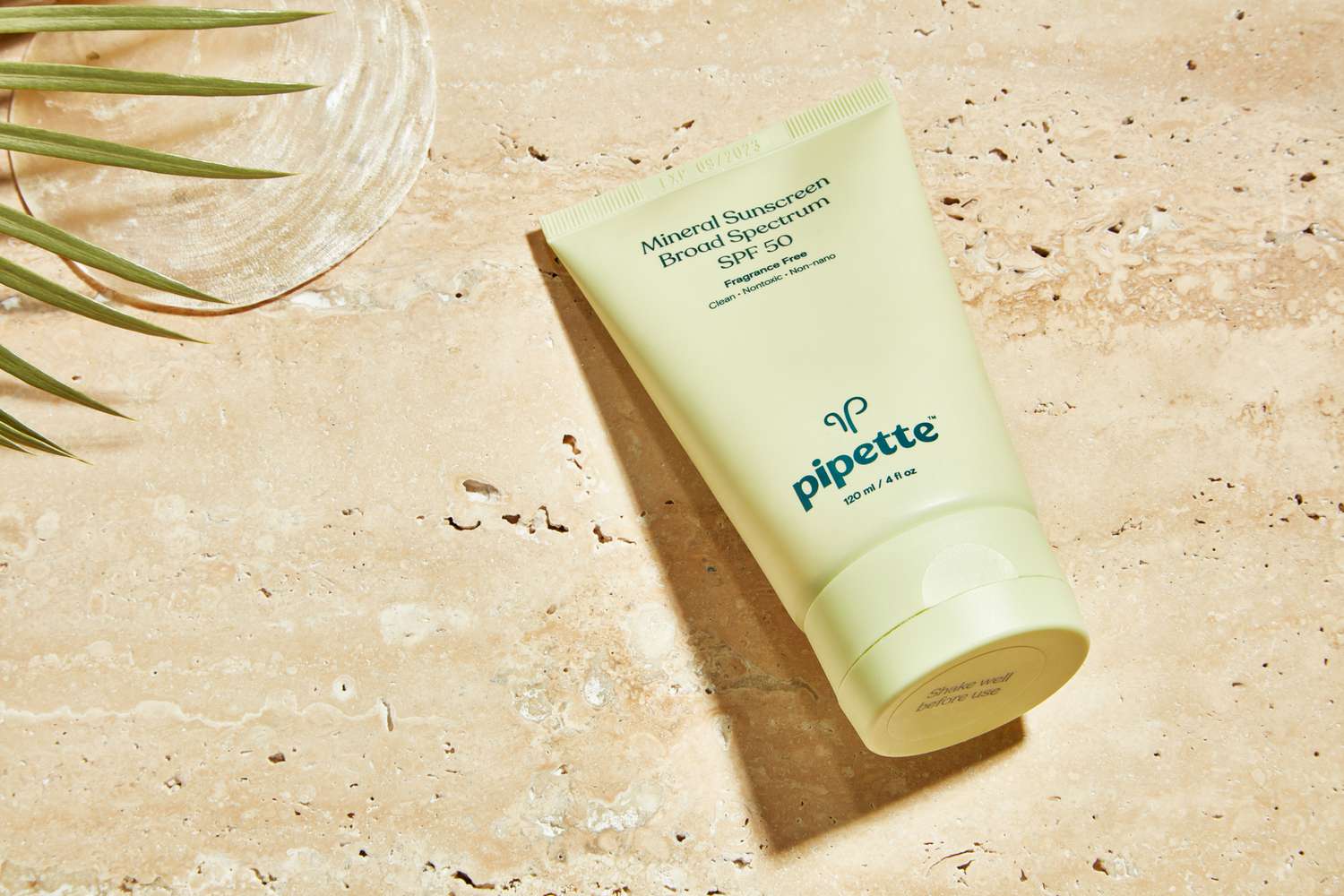 Pipette Mineral Sunscreen displayed on a sandy background next to a leafy plant and seashell