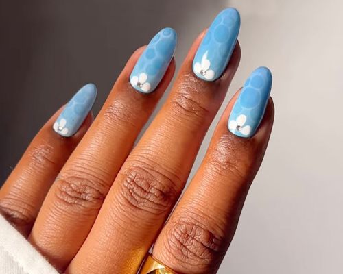 Light blue nails with a pool surface effect and white floral details at the cuticle.