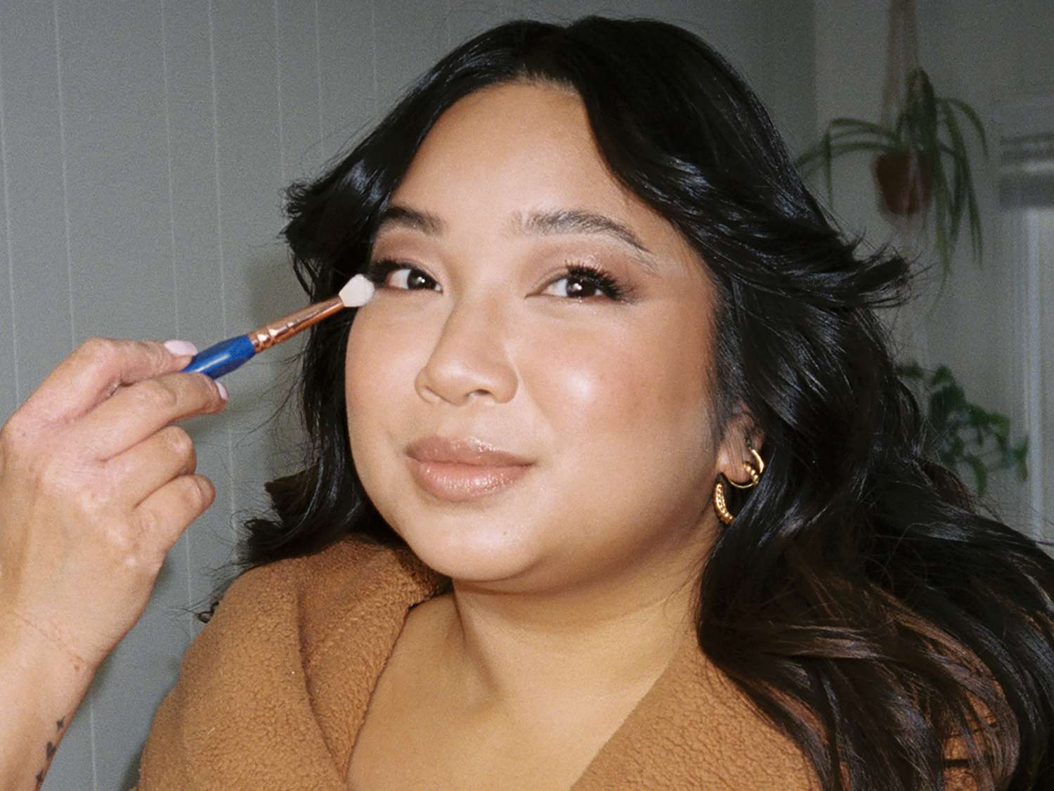 The author in a tan robe, her hair full and bouncy, with a makeup artist applying eyeshadow to her face