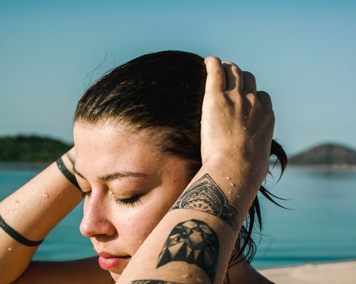 girl with wet hair near a body of water, with tattoos on both arms