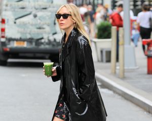 Chloe Sevigny wears a black vinyl jacket, floral mini dress, and sunglasses while carrying a green matcha