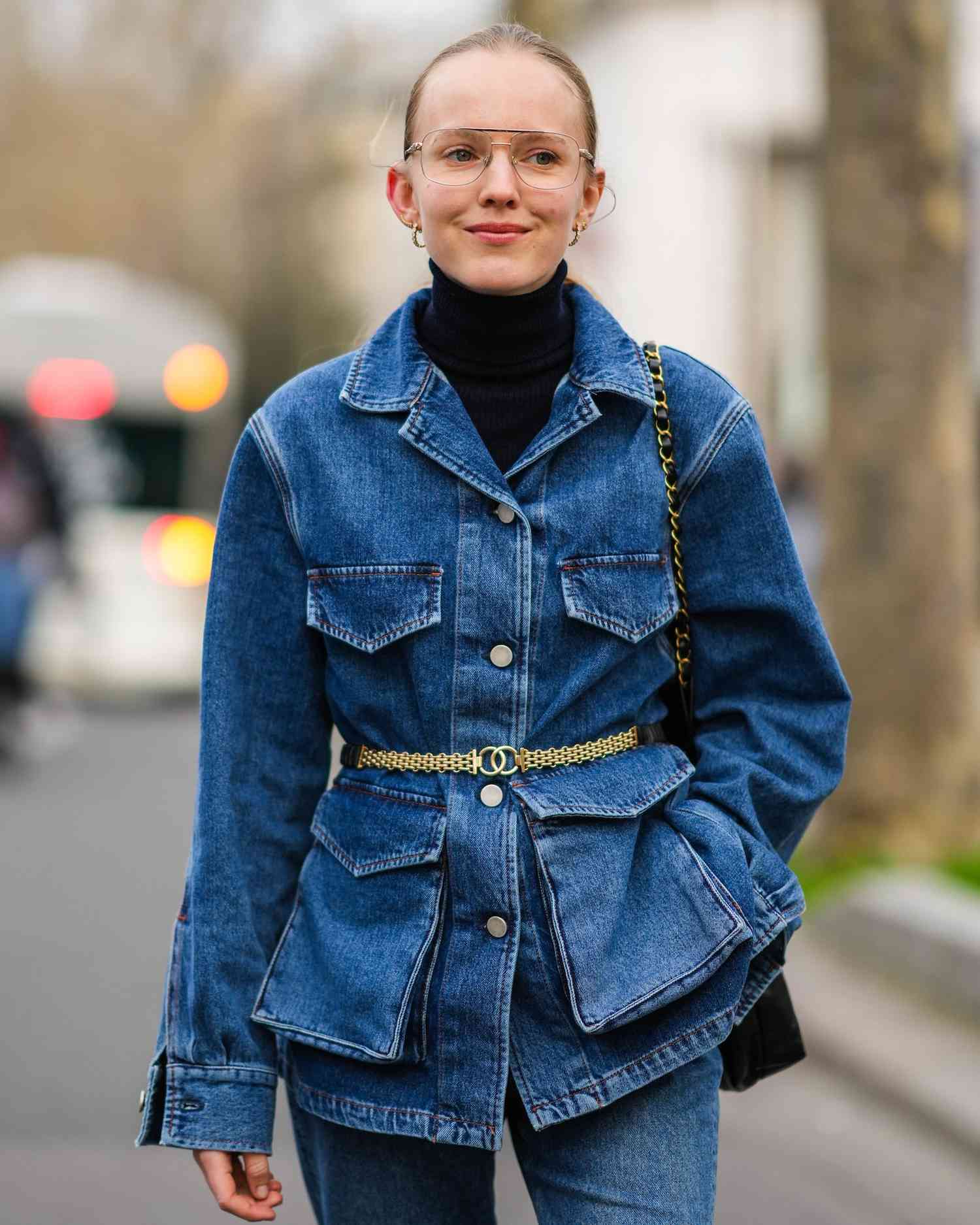 Alexandra Carl wears a black turtleneck, denim jacket, jeans, gold Chanel belt and black Chanel shoulder bag, and aviator eyeglasses