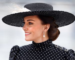 Kate Middleton wears a radiant makeup look, updo hairstyle, pearl drop earrings, black hat, and polka-dot dress