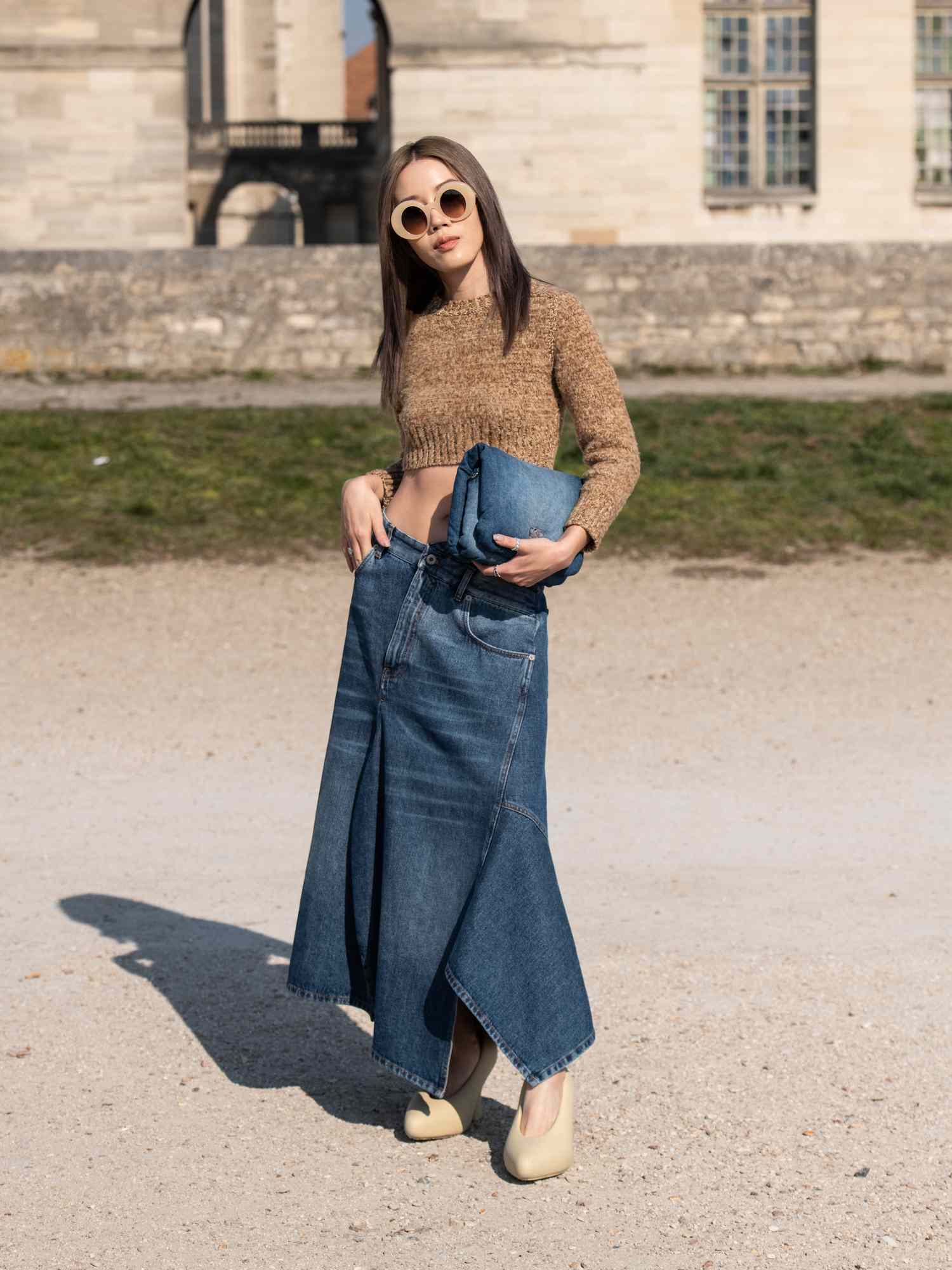 Jenny Tsang wears a denim skirt, denim handbag, and beige cropped sweater with oversized round sunglasses