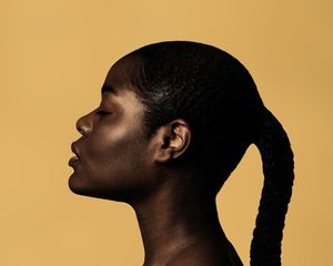 braided woman taking pictures beside yellow wall