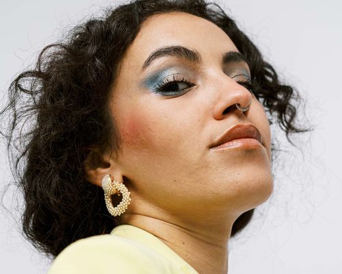 woman with blue eyeshadow and septum nose piercing wearing a yellow blazer