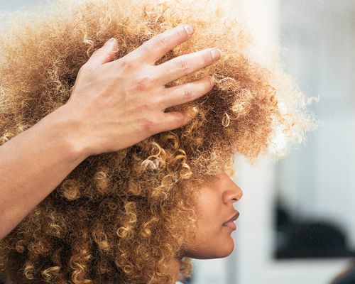 Hairstylist shapes a woman's afro in a salon.