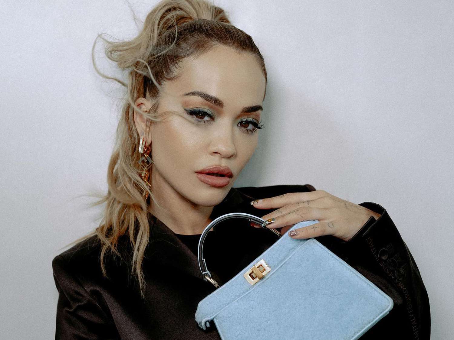 RIta Ora with a high pony tail and holding a blue denim bag