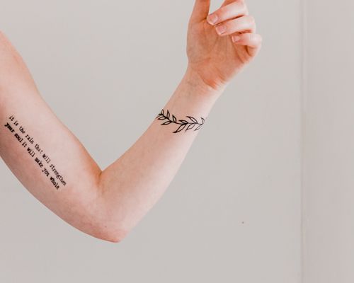 arm with two tattoos, one of words and the other a bracelet of leaves