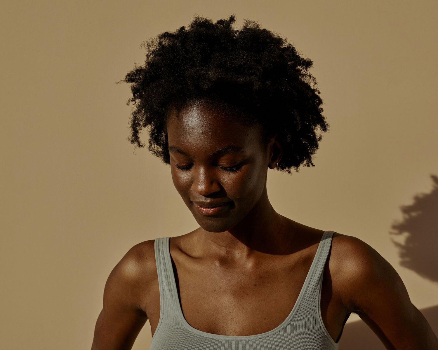 Woman with radiant skin, natural curls, and small amount of acne gazes downwards