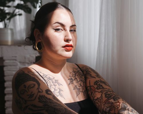 woman sitting next to window with tattoos on arms