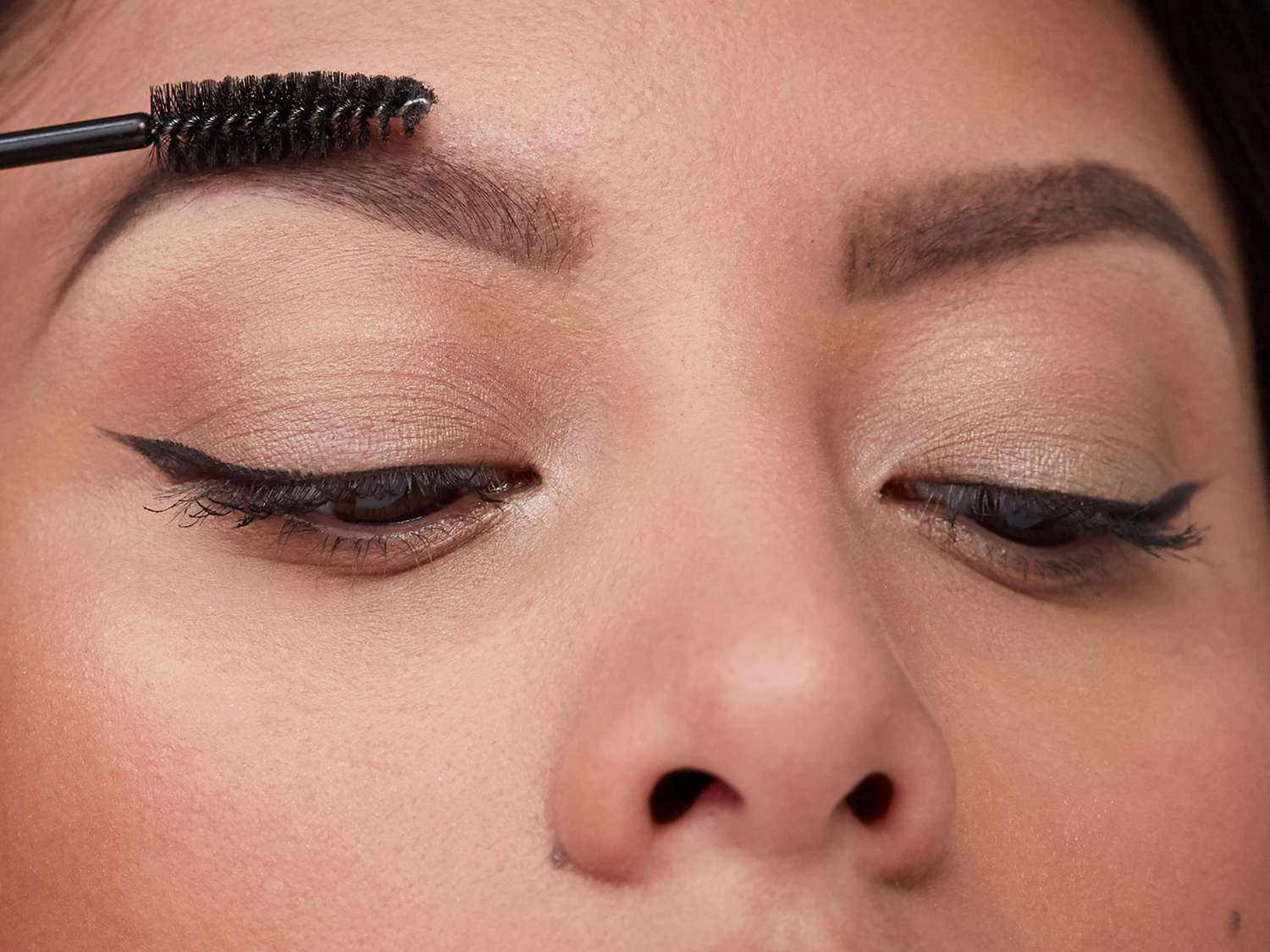 Close up of woman with winged liner and fluffy eyebrows being groomed with spoolie brush