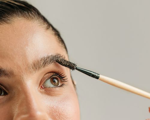 Close up of a brow brush in a woman's eyebrow against a gray background