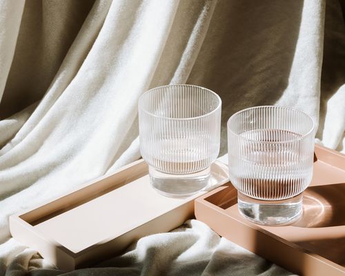 Two glasses of water on trays with textured fabric in the background