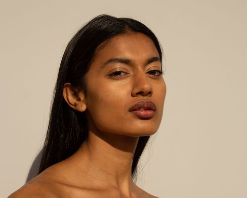 woman with olive skin standing against tan background