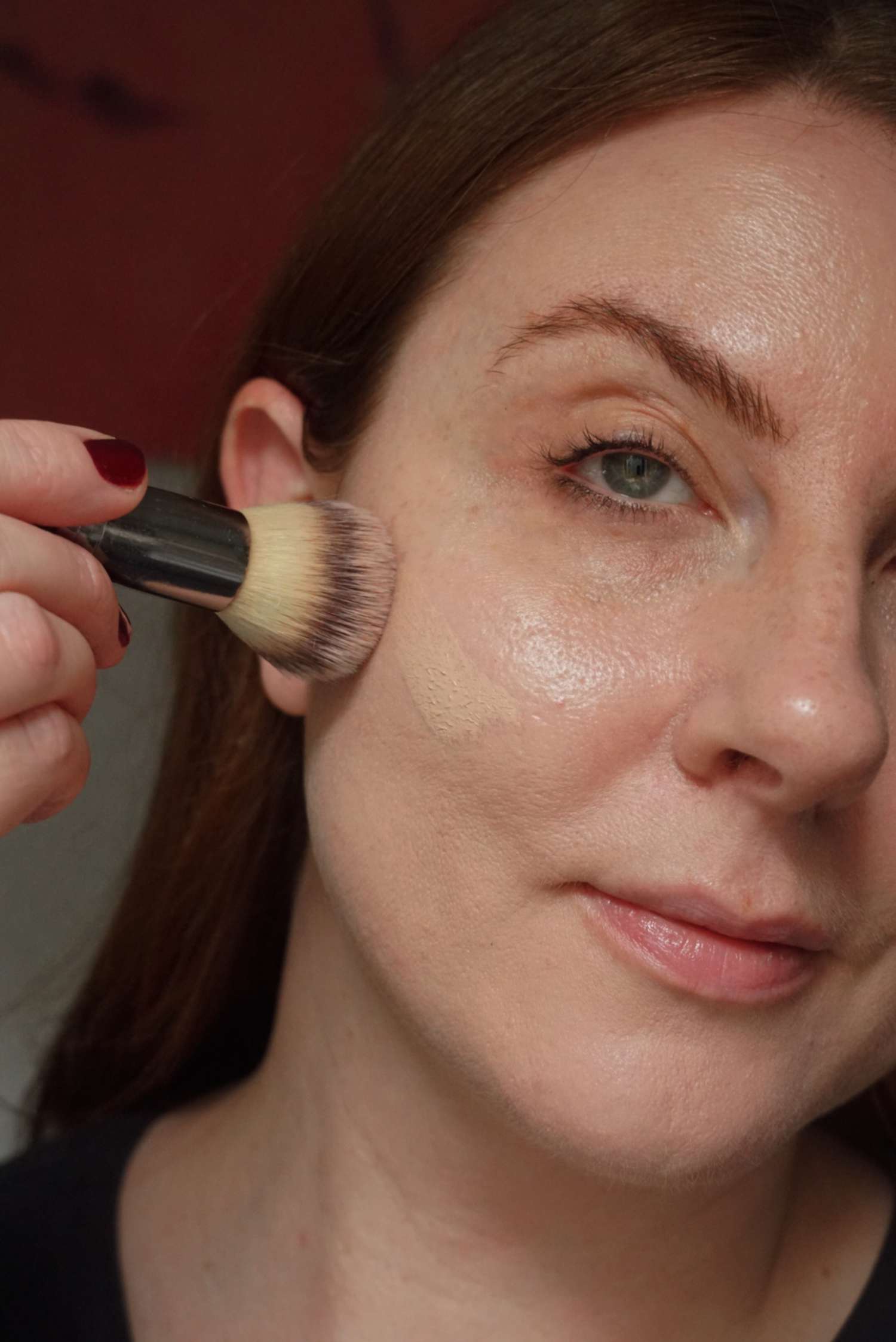 woman applying foundation to the cheek with a fluffy foundation brush