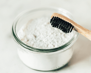 A bowl of baking soda with a black bristle toothbrush propped up on the side