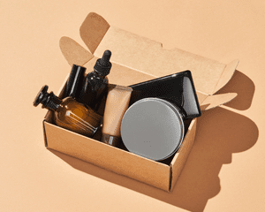 Close up of a brown cardboard box with makeup and beauty products in it, on a beige background.