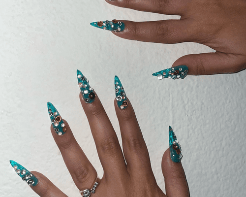 Close up of long blue nails with multicolor rhinestone crystals on each nail. 