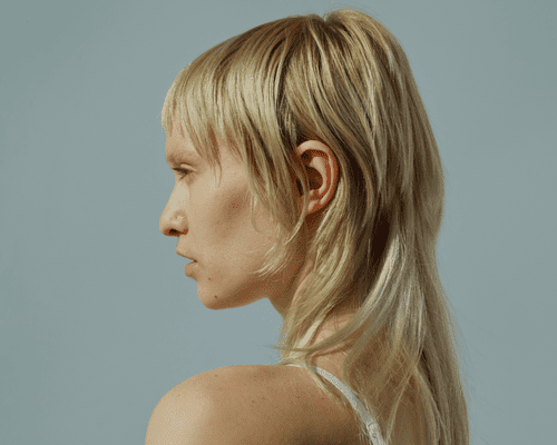 A close up, side profile of a model with a blonde mullet.